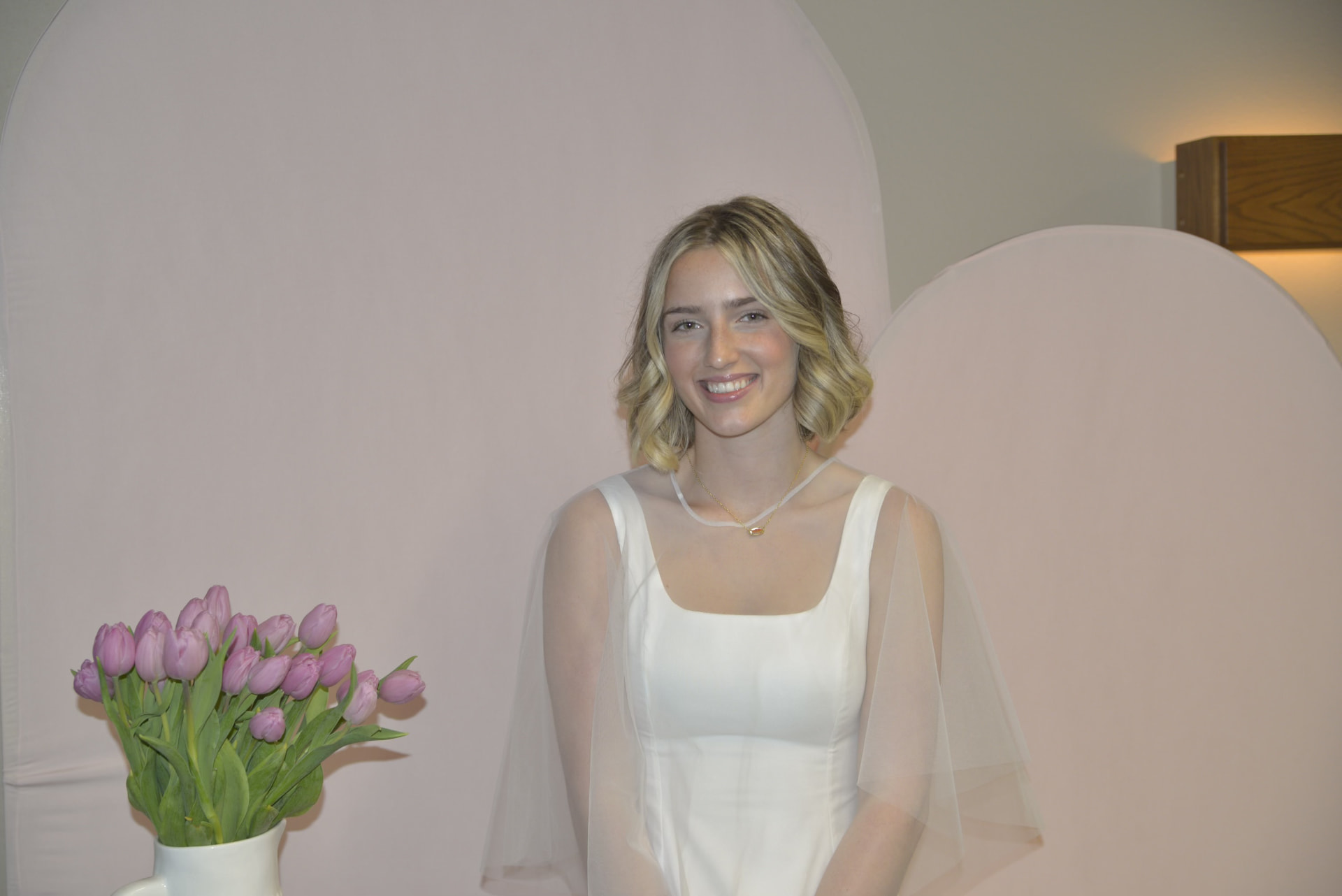 Lilly smiling beside a vase of pink tulips